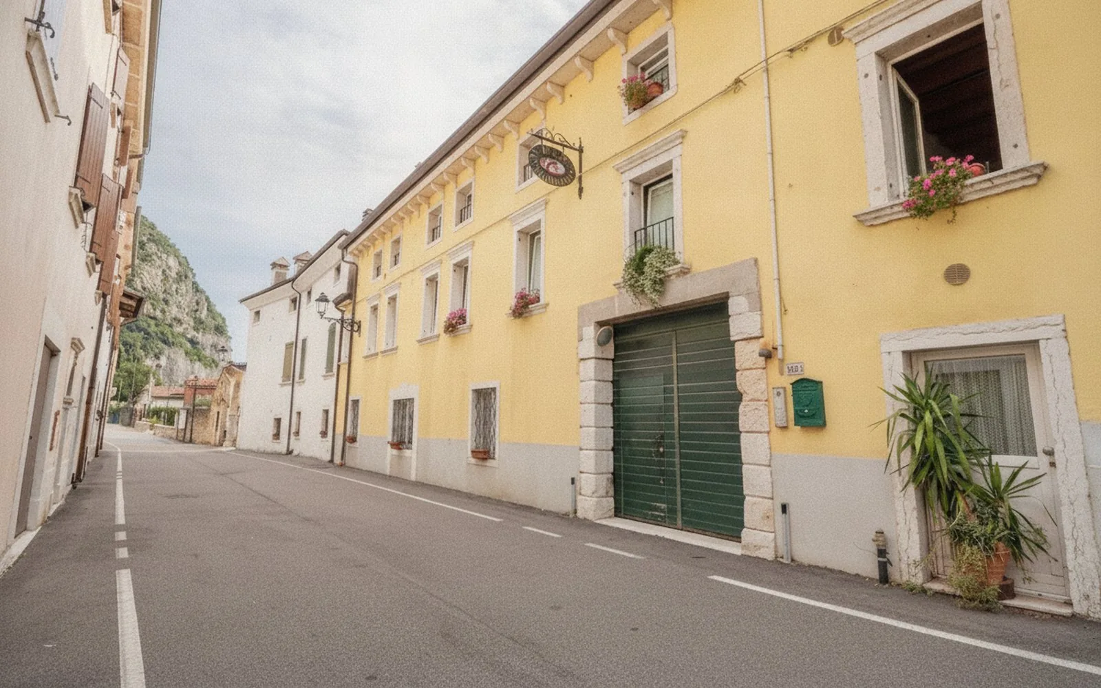 La via del centro di Ceraino con la facciata gialla della corte e la parete rocciosa sullo sfondo